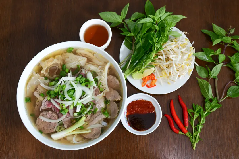 A complete and beautifully presented Southern-style Vietnamese beef pho set, including the main soup bowl, plate of herbs and sprouts, dipping sauces, and fresh chilies. (1)