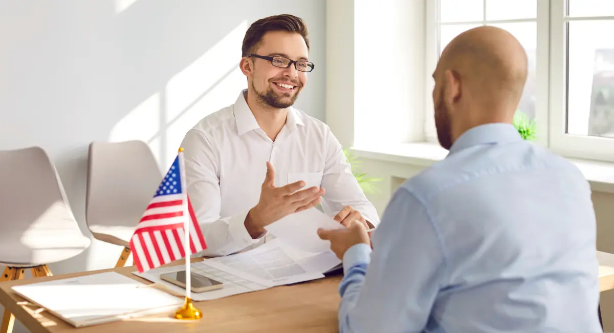 Consular officer providing assistance to an individual across a service counter inside an embassy or consulate setting.