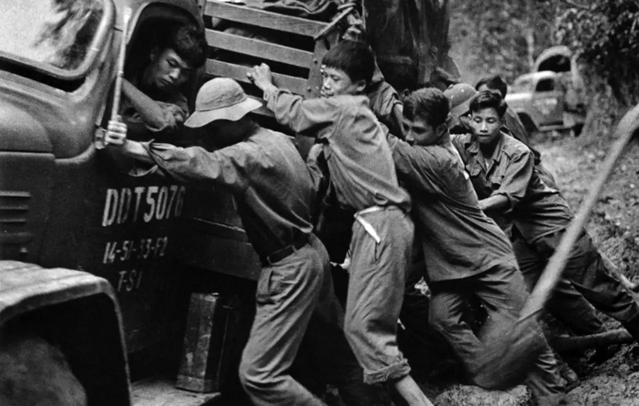 Determined PAVN soldiers carrying supplies through the dense, muddy jungle terrain of the Ho Chi Minh Trail during the Vietnam War.