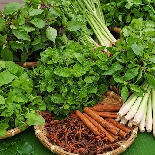 Fresh Vietnamese herbs like mint, basil, cilantro, and lemongrass, alongside dried star anise and cinnamon sticks arranged on woven bamboo trays and banana leaves.