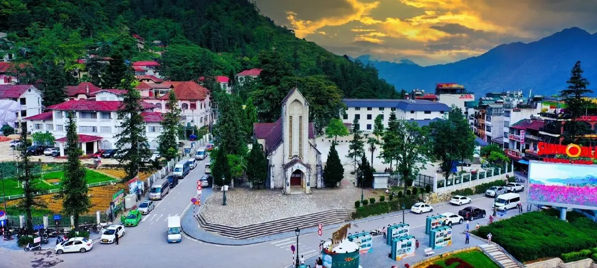 Street in Sapa town, Vietnam, featuring several multi-story hotels lining a sloping road, with mountains in the background.
