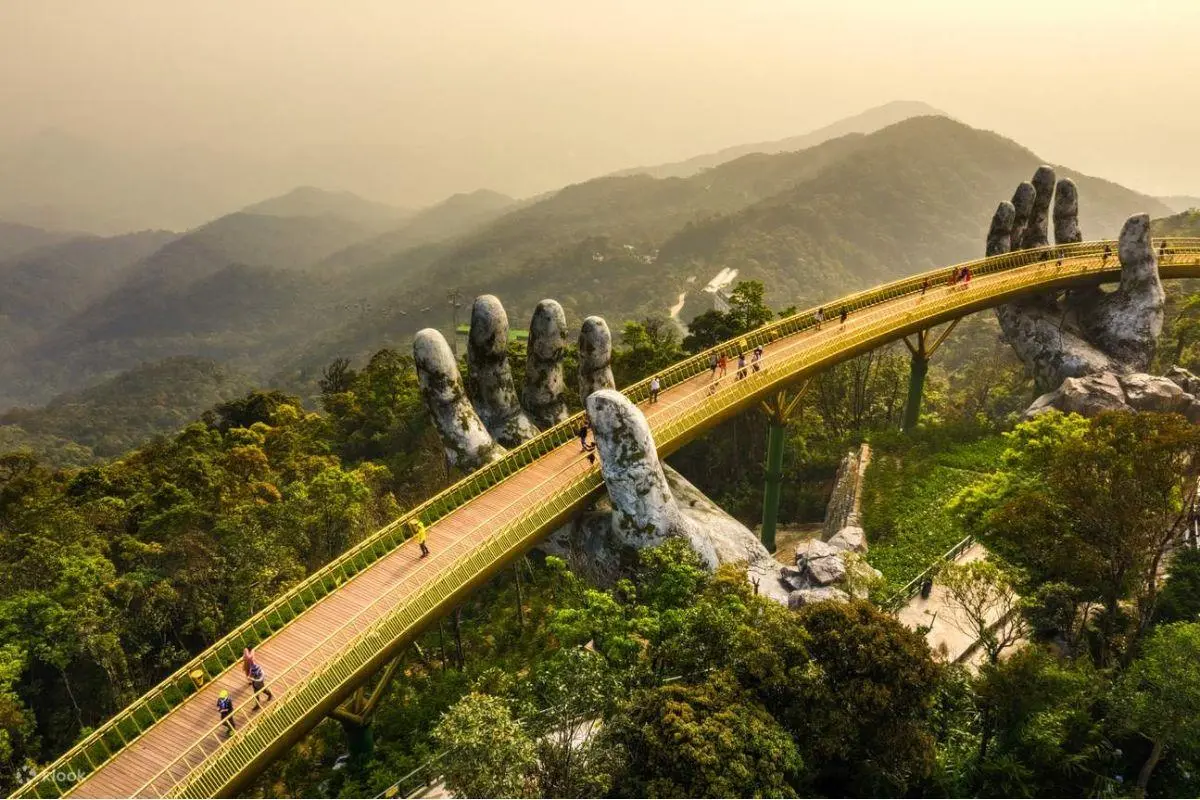 Tourists walking on the iconic Golden Bridge held by giant stone hands at Ba Na Hills Vietnam.