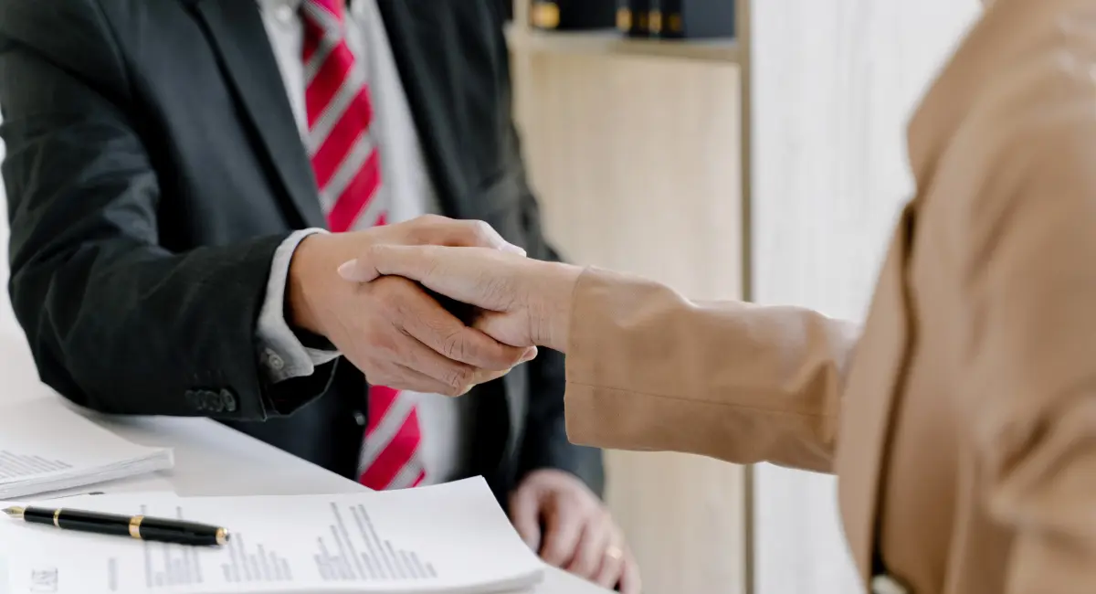 Two officials in professional attire shaking hands in a formal meeting room, symbolizing diplomatic relations.