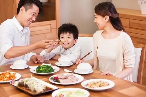 Vietnamese family (father, mother, son) happily eating a meal together, sharing dishes at a table