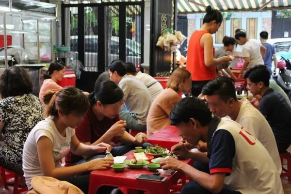 A bustling Vietnamese street food restaurant with people eating at red plastic tables