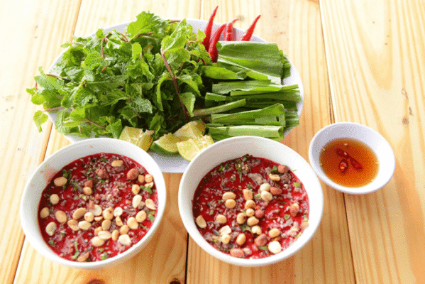 A vibrant Vietnamese meal two bowls of Tiet Canh (blood pudding) with peanuts, served with fresh herbs, chilies, lime, and dipping sauce
