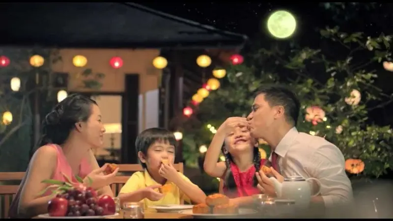 Happy Vietnamese family celebrating Mid-Autumn Festival, eating mooncakes together under the moonligh