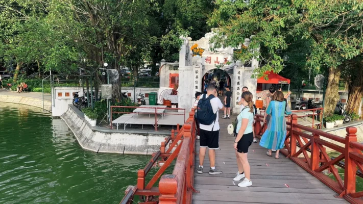 Tourists walk on a red wooden bridge towards a