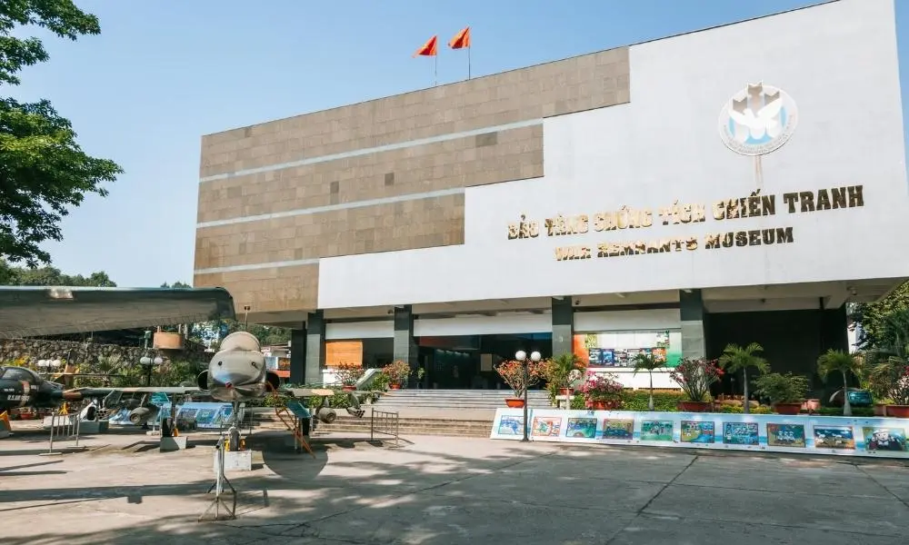 Visitors viewing large military hardware exhibits in the courtyard of the War Remnants Museum Vietnam, signifying its historical impact