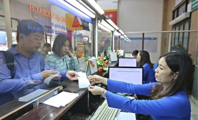 A bank teller assists a male customer, handing him paperwork over a counter