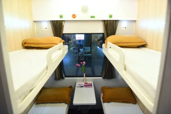 Interior of a train sleeper cabin with bunk beds, a central window, and a small table with flowers