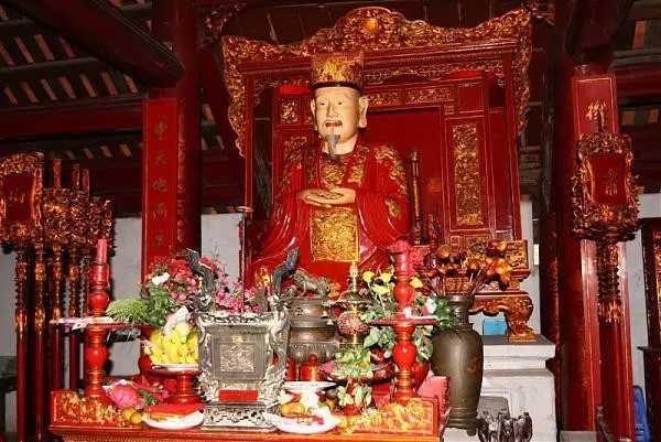 Statue of Confucius in red and gold robes on an altar, with offerings, at the Temple of Literature
